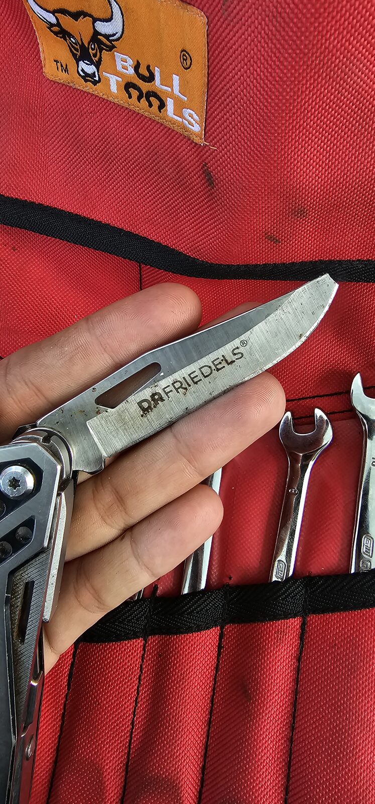 The DRFRIEDELS-branded blade from Lyn's original multi-tool, photographed in her Bull Tools work bag alongside a set of combination spanners